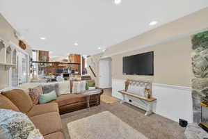 Carpeted living area featuring wainscoting, recessed lighting, and a stone-clad fireplace
