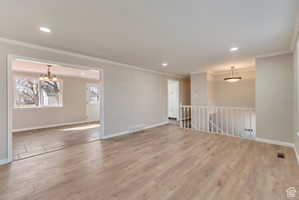 Spare room with light wood-style floors, ornamental molding, and suspended lighting