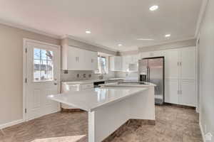 Kitchen with white cabinets, stainless steel appliances, a center island, crown molding, and tasteful backsplash