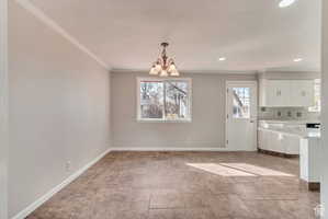 Unfurnished dining area with a chandelier, crown molding, and healthy amount of natural light