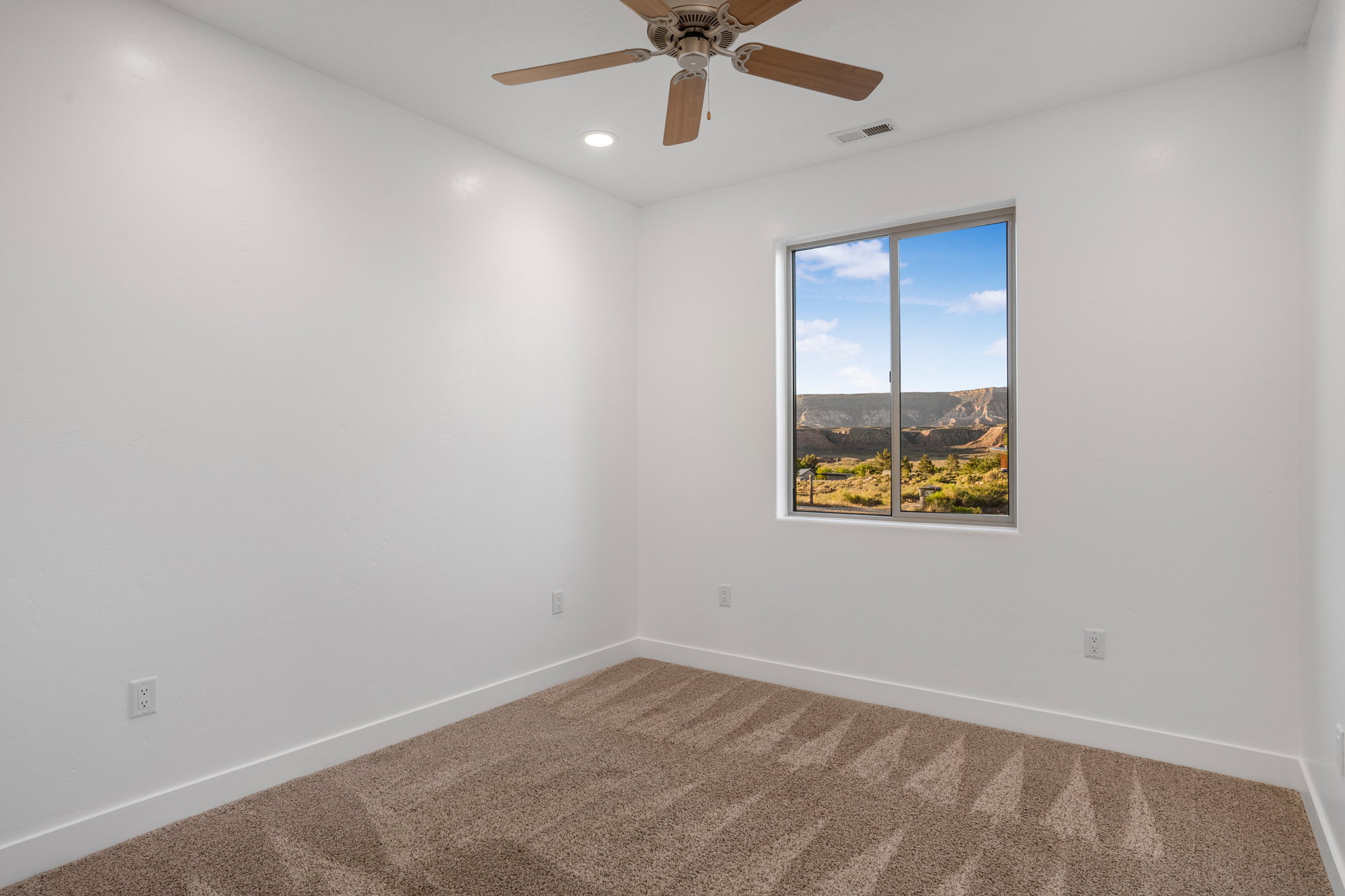 Bedroom featuring a window with a desert mountain landscape, neutral carpet flooring, recessed lighting, and a ceiling fan