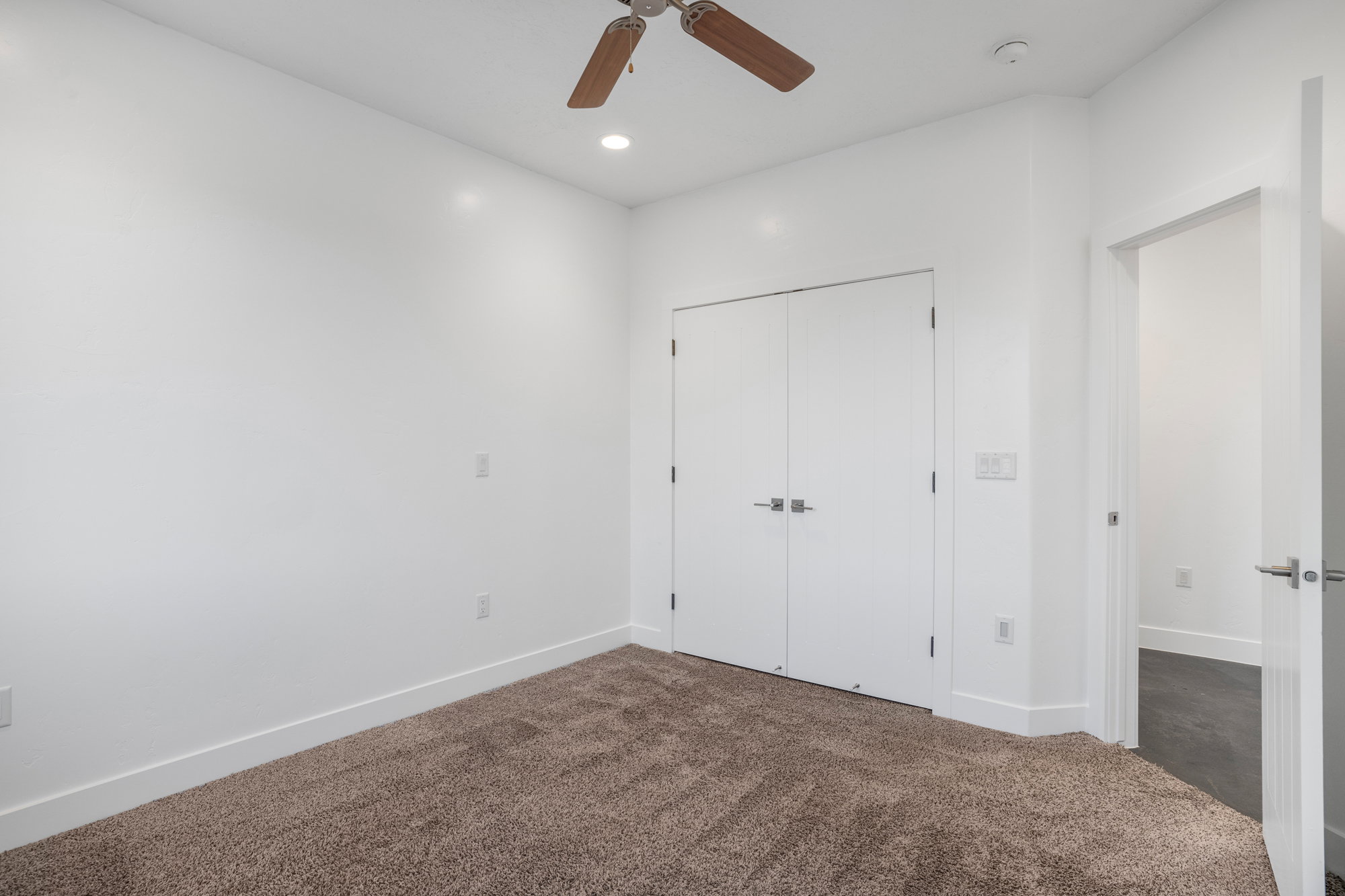 Spacious interior room featuring plush brown carpeting, recessed lighting, and a ceiling fan
