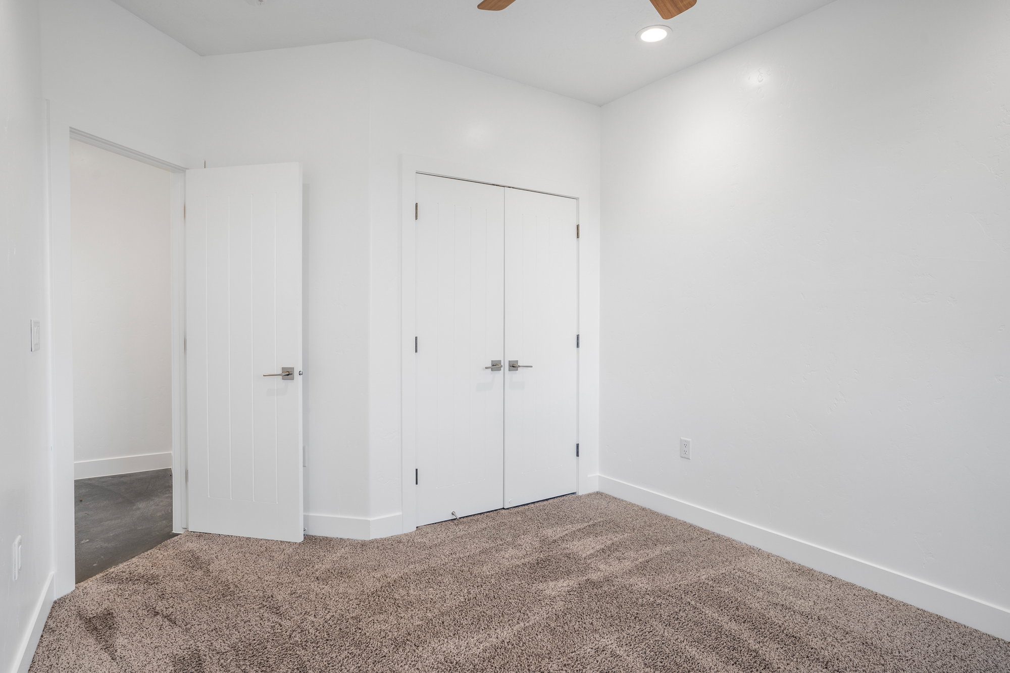 Neutral-toned carpeting paired with white walls, a white paneled door with brushed nickel hardware, and a closet with bifold doors