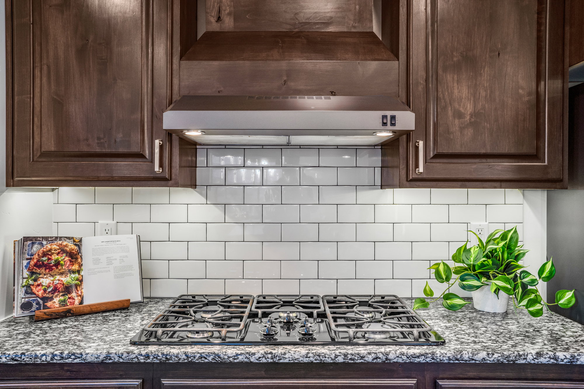 Kitchen featuring a built-in gas cooktop, granite-style countertops, white subway tile backsplash, dark wood cabinetry, and a stainless steel range hood