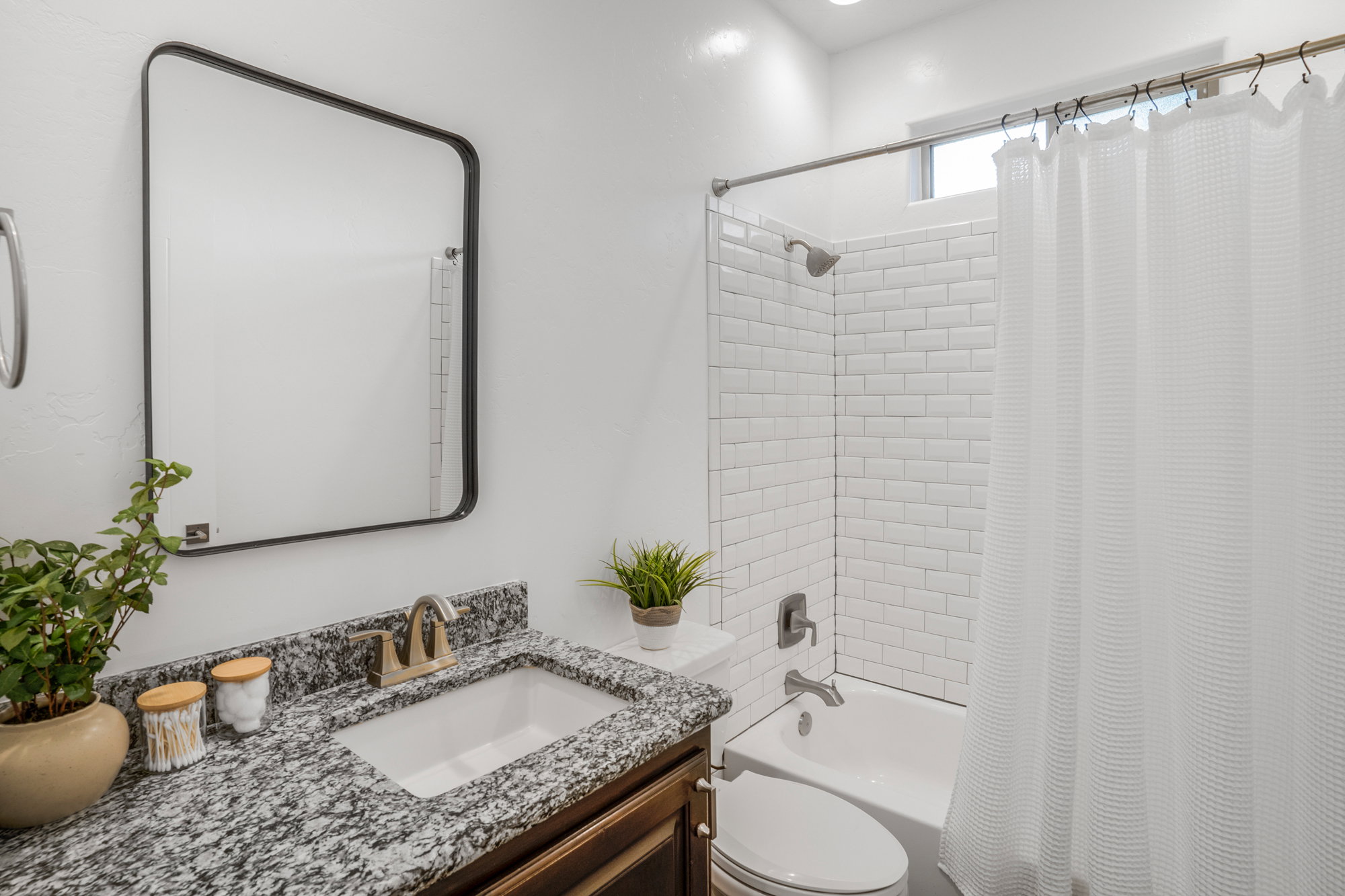 Bathroom featuring a white subway tile shower surround, a built-in tub, a vanity with a granite-style countertop, an undermount sink with a bronze-tone faucet, and a contemporary framed mirror