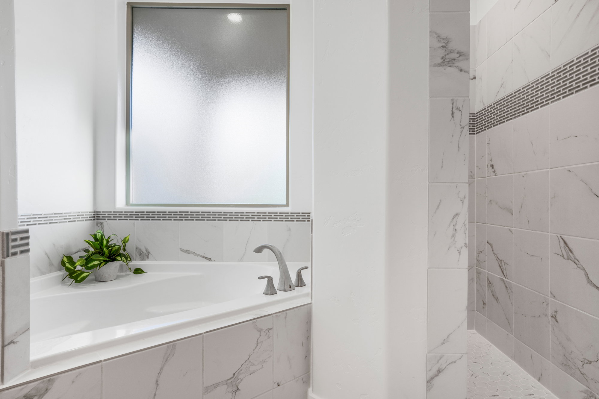 Recessed soaking tub with brushed nickel fixtures set against white and gray veined tile surround