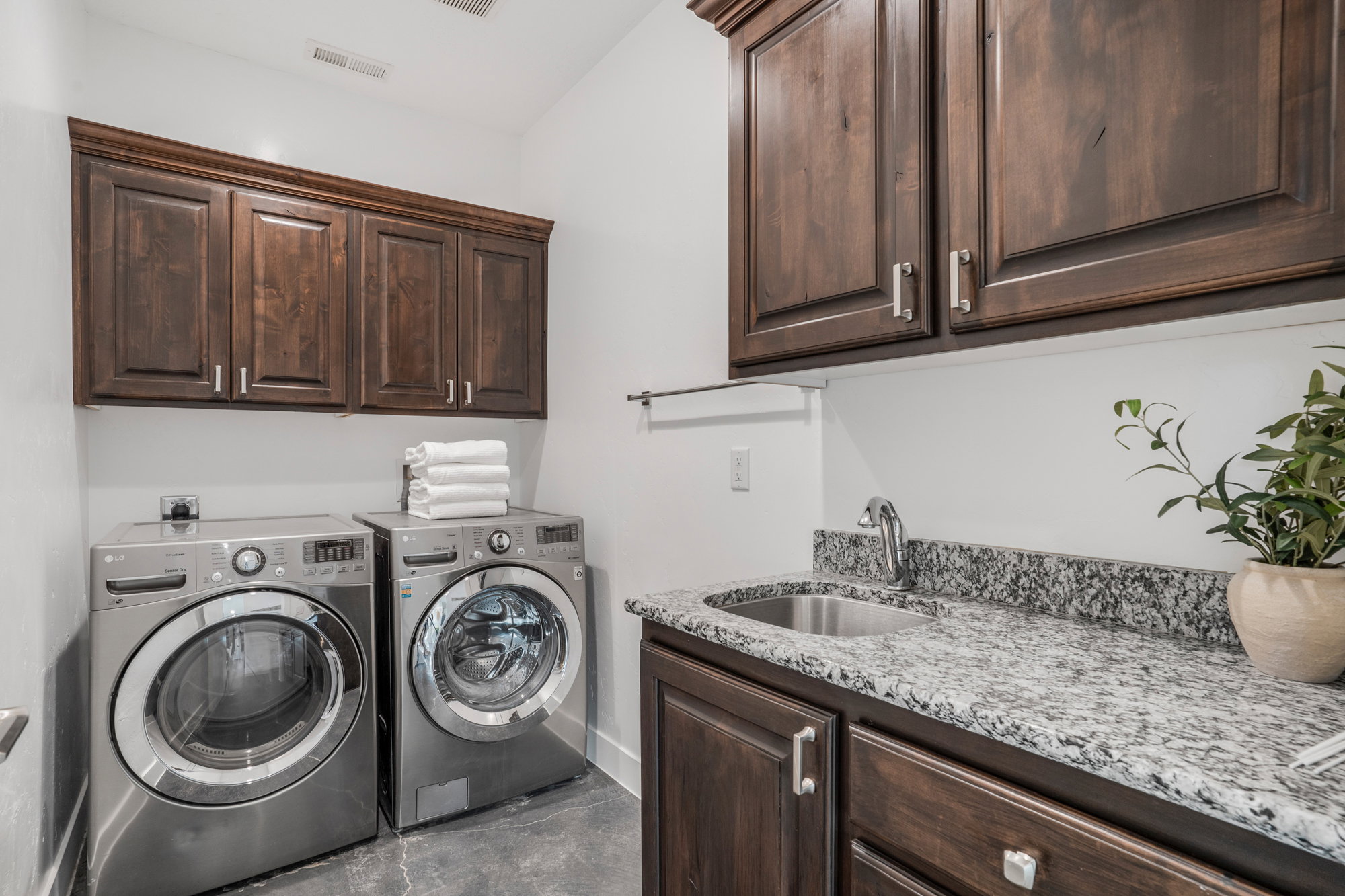 Laundry area featuring dark wood-finish cabinetry, a stainless steel utility sink, and speckled stone countertops