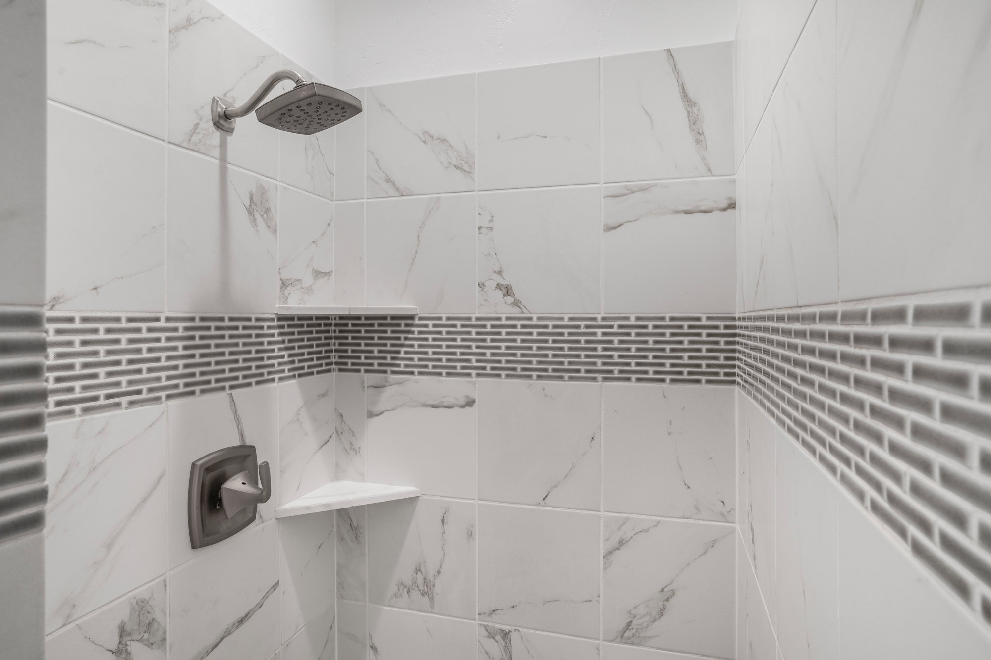 Shower enclosure featuring large format white tiled walls with subtle veining