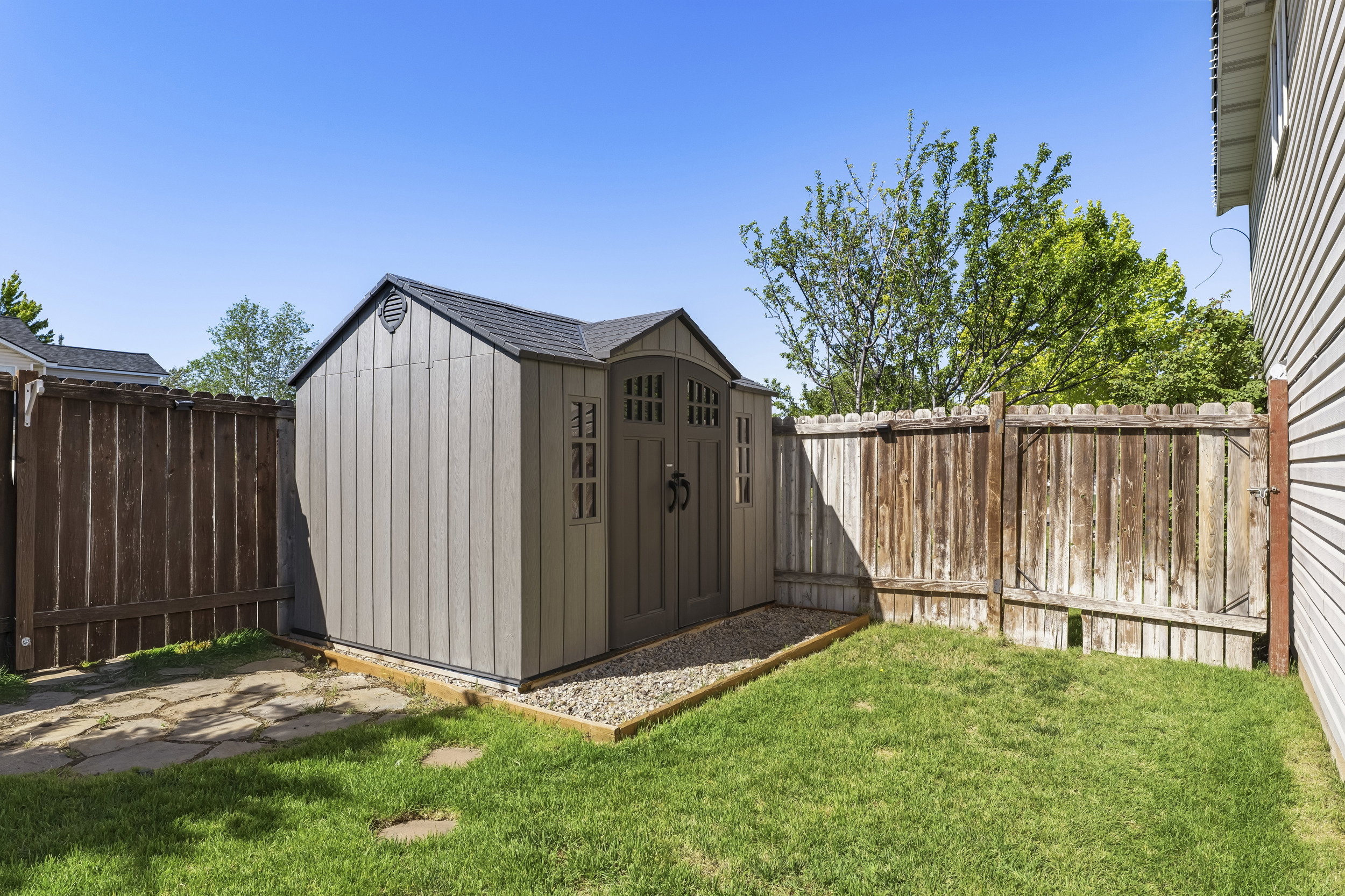Backyard featuring a gray outdoor storage shed with double doors and decorative windows, surrounded by a wood fence