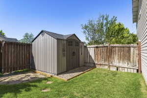 Backyard featuring a gray outdoor storage shed with double doors and decorative windows, surrounded by a wood fence