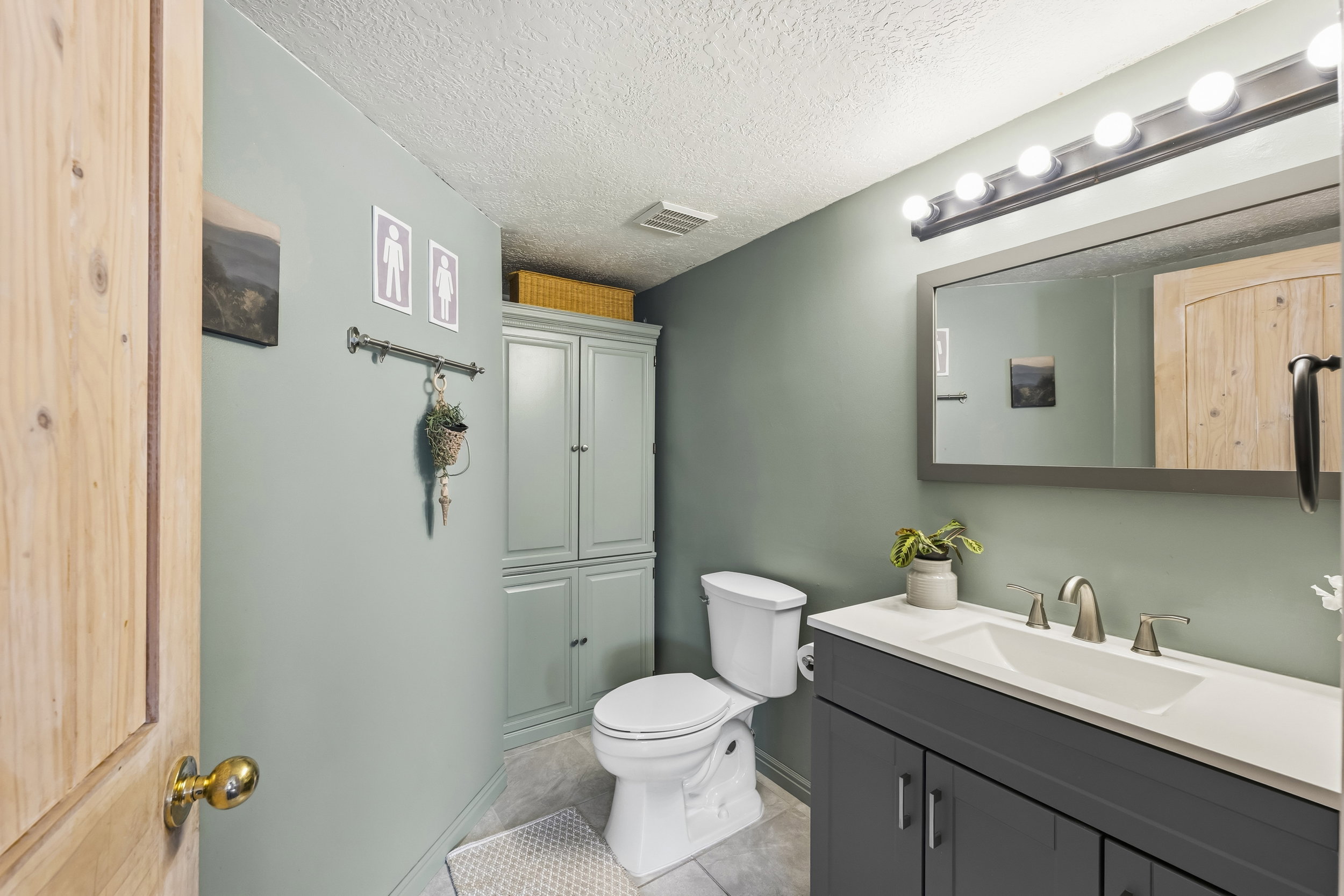 Bathroom featuring a dark gray vanity with a single sink, an overhead vanity light fixture, and a built-in storage cabinet