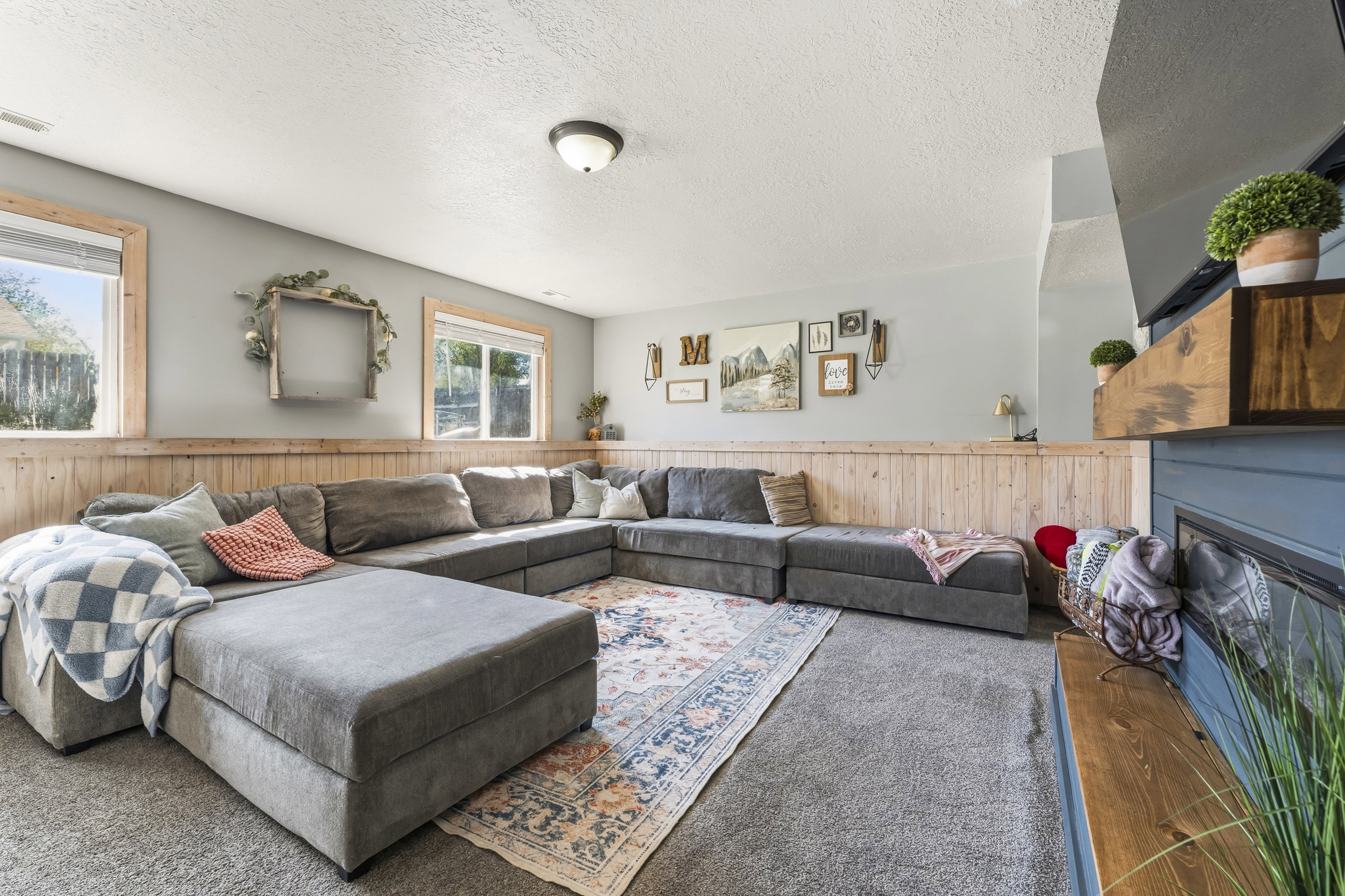 Carpeted recreation room featuring wood-paneled wainscoting, light gray walls, and multiple windows with wood trim