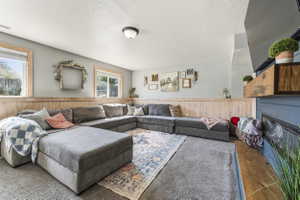 Carpeted recreation room featuring wood-paneled wainscoting, light gray walls, and multiple windows with wood trim