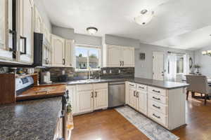 Kitchen featuring cream-painted cabinetry, dark speckled countertops, a stone tile backsplash, stainless steel appliances, and wood-finish flooring