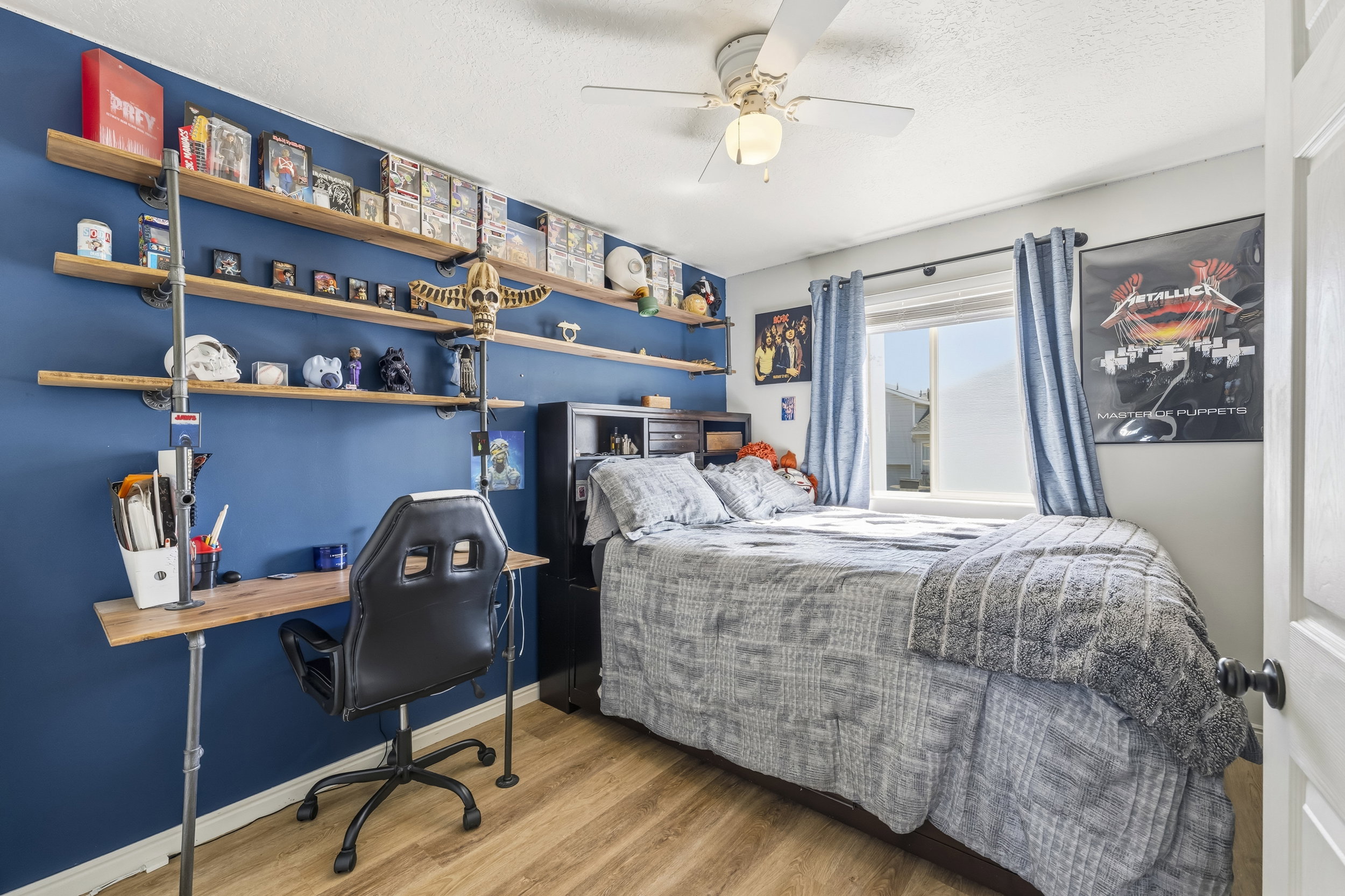 Bedroom featuring wood-finish flooring, a ceiling fan with integrated lighting, and a window with blue curtains