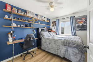 Bedroom featuring wood-finish flooring, a ceiling fan with integrated lighting, and a window with blue curtains