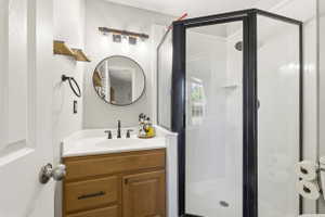 Full bathroom featuring a walk-in shower with black framing, a single vanity with wood-finish cabinetry, a white countertop, and a circular mirror