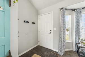 Entryway featuring a white paneled door, dark tile flooring, and a corner window arrangement
