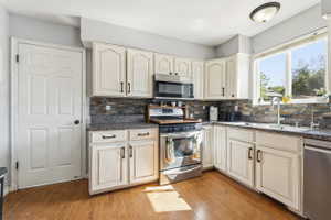 Kitchen featuring wood-finish flooring, white cabinetry with dark hardware, stone-look countertops, and a full-height stacked stone backsplash