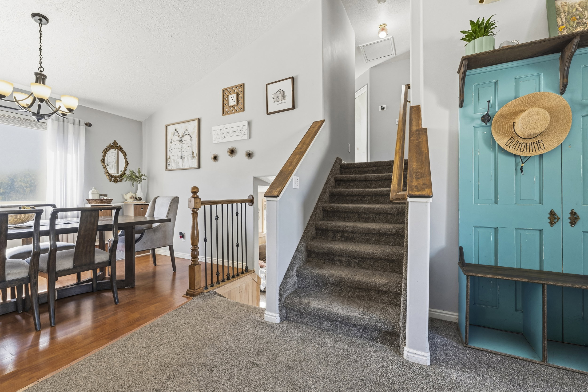Inviting entryway featuring carpeted stairs with wood handrails, a dining area with wood-finish flooring, a contemporary chandelier, and a large window