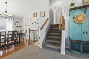 Inviting entryway featuring carpeted stairs with wood handrails, a dining area with wood-finish flooring, a contemporary chandelier, and a large window