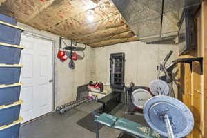 Versatile basement area featuring concrete walls, exposed ceiling insulation, a white paneled door, and durable rubber mat flooring