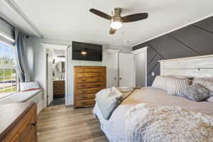 Bedroom featuring wood-finish flooring, a decorative accent wall, and a ceiling fan with integrated lighting