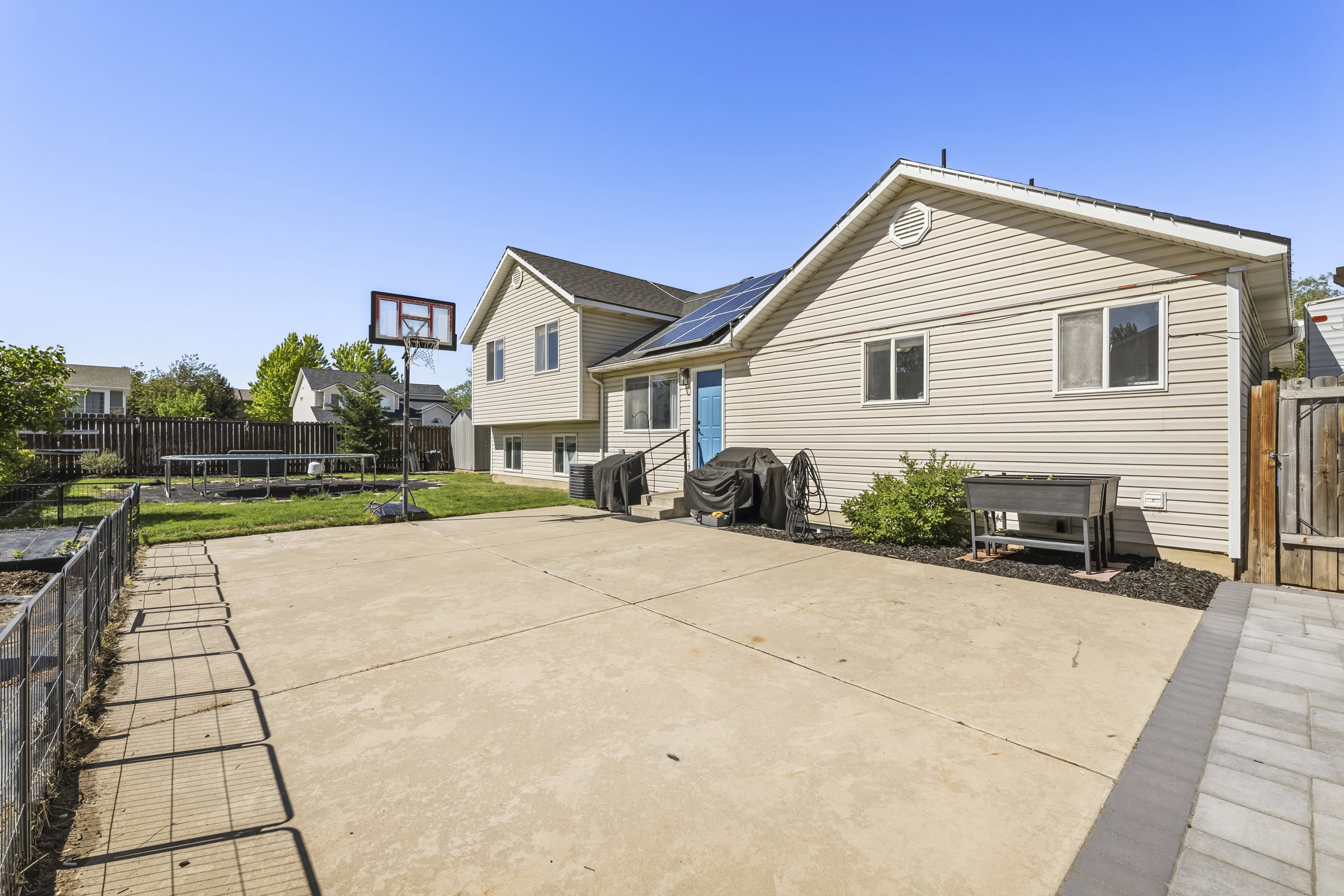 Expansive concrete patio with a paved border, leading to a manicured lawn and a fenced garden area
