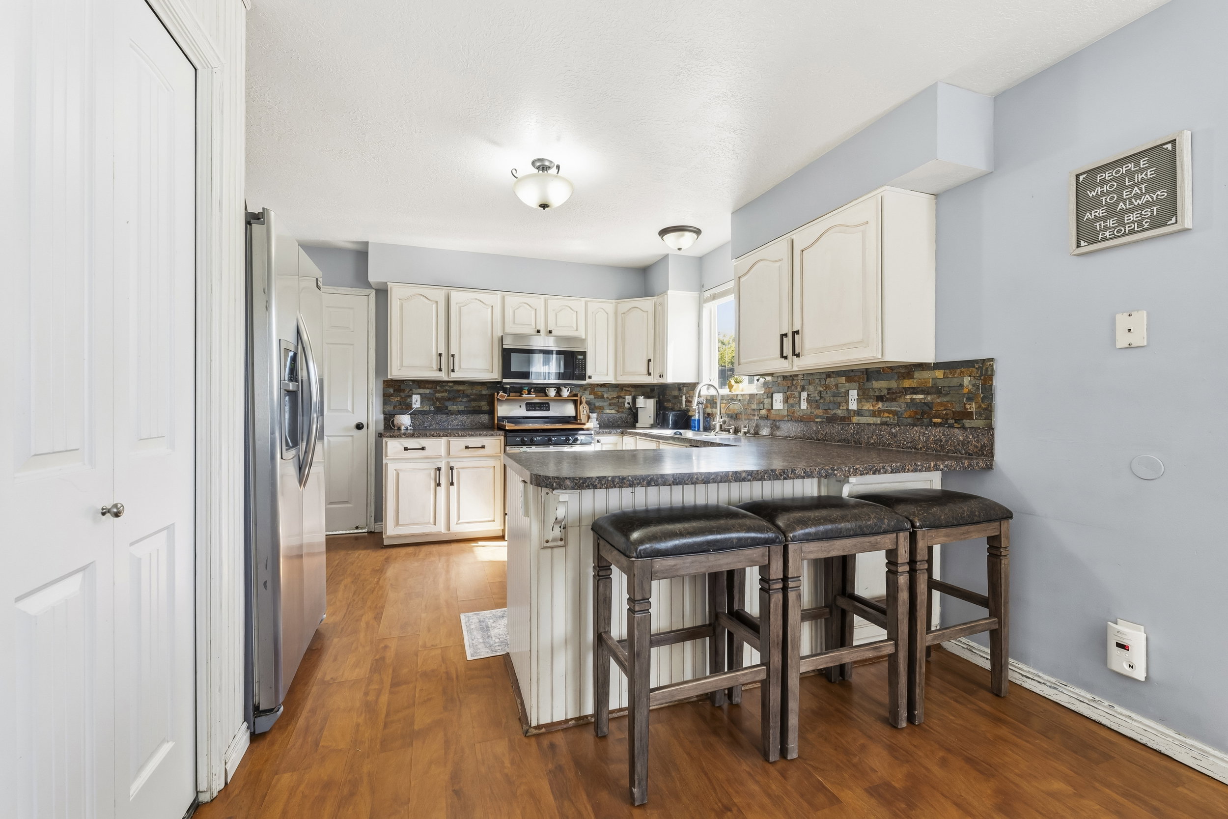 Kitchen featuring wood-finish flooring, white cabinetry, stainless steel appliances, and dark countertops with a tiled backsplash