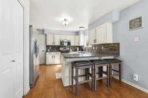 Kitchen featuring wood-finish flooring, white cabinetry, stainless steel appliances, and dark countertops with a tiled backsplash