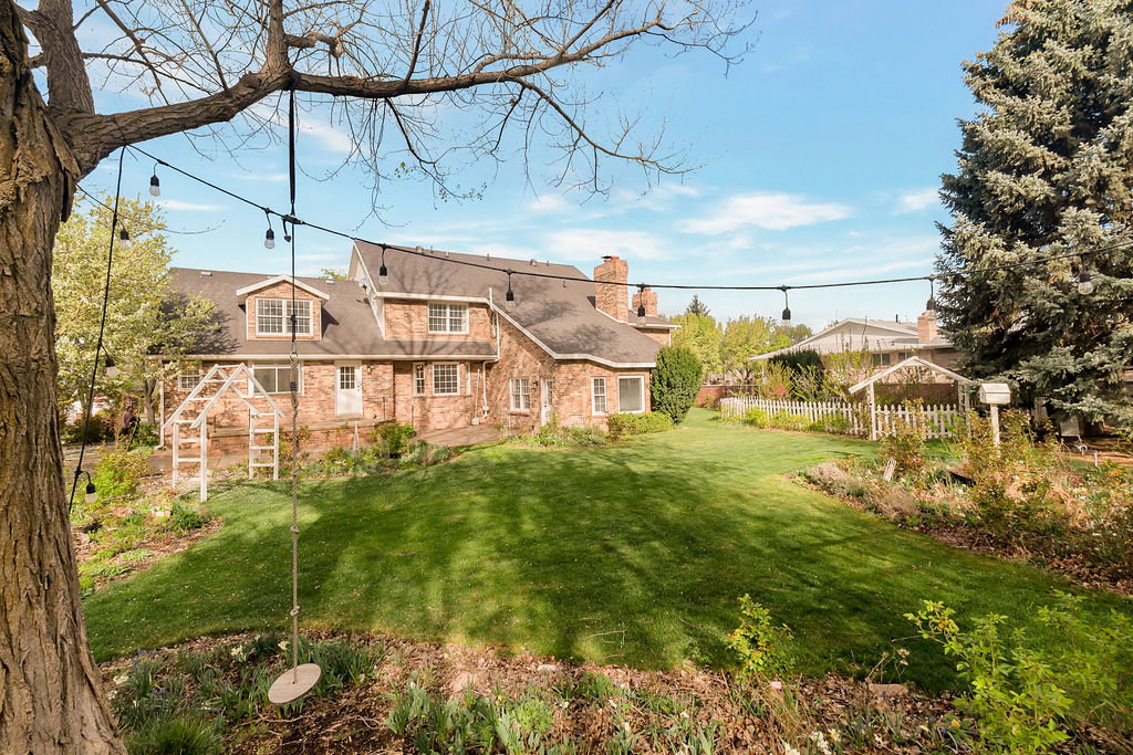 Expansive backyard featuring a lush lawn, mature trees, and string lighting