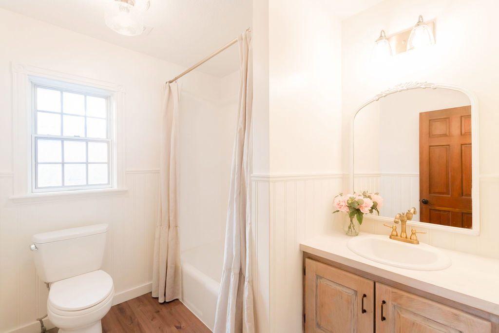 Full bathroom featuring a window with grid patterns, a white tub with shower, and wood-finish flooring