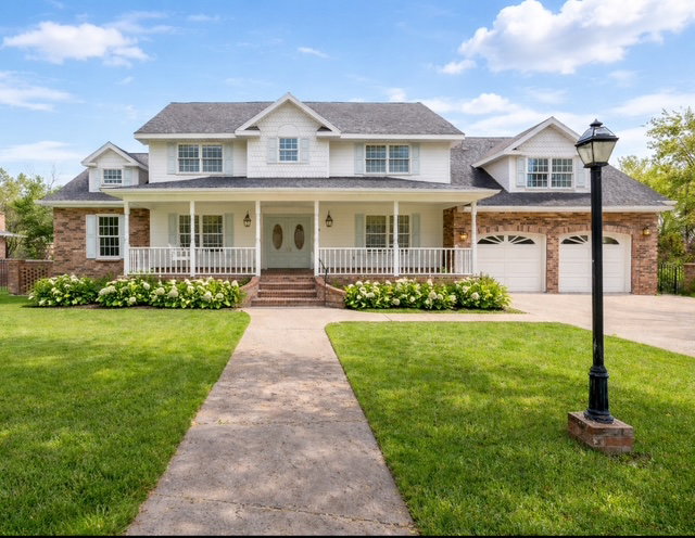 Traditional-style residence featuring a brick and white siding exterior, a covered front porch with white railings, and a double-door entry