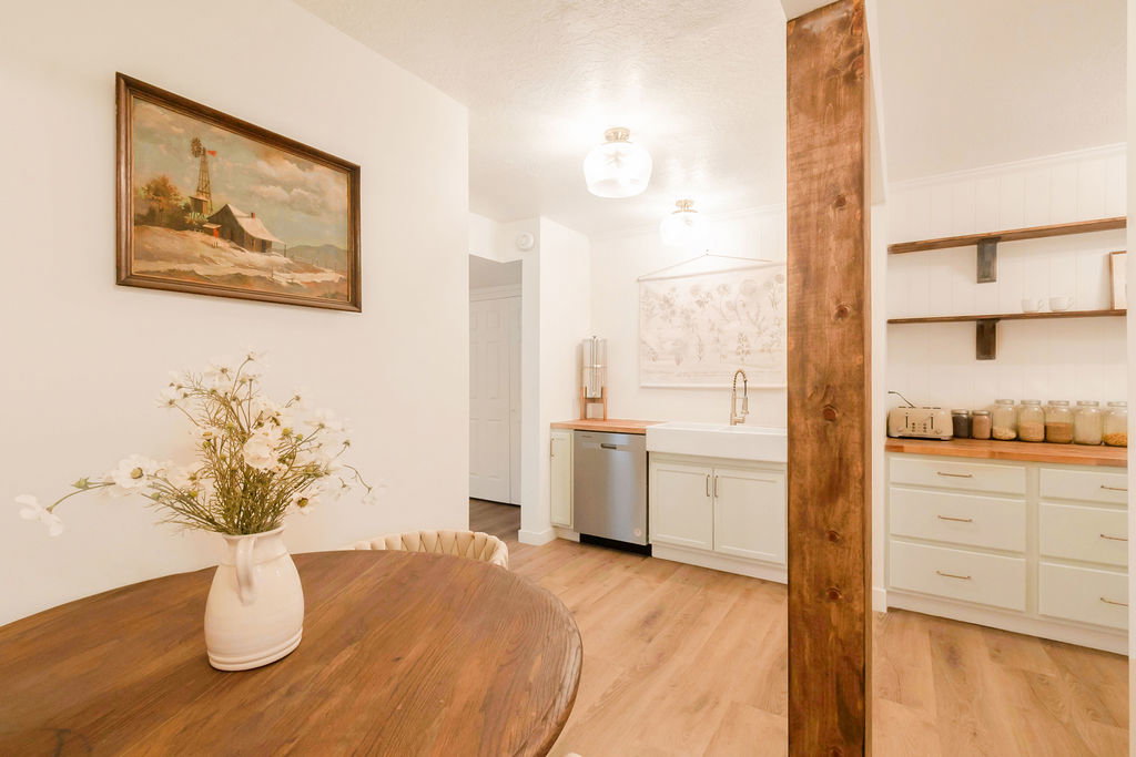 Kitchen area featuring wood-finish flooring, white cabinetry with silver hardware, butcher block countertops, a farmhouse sink with a gooseneck faucet, and open shelving with metal brackets