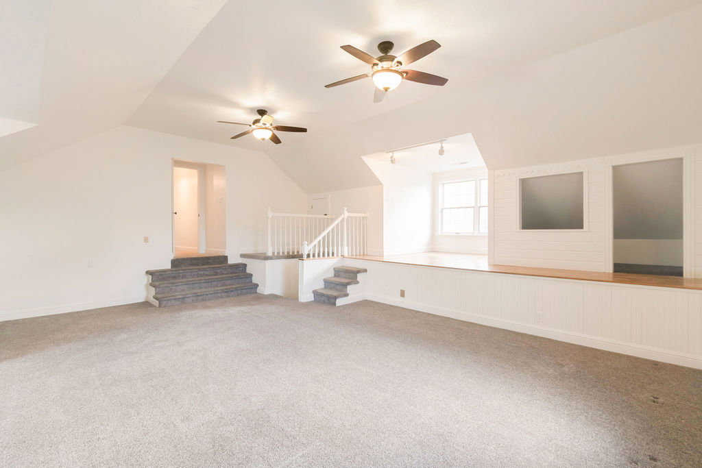 Spacious upper-level room featuring angled ceilings, light gray carpet, and two ceiling fans with integrated lighting