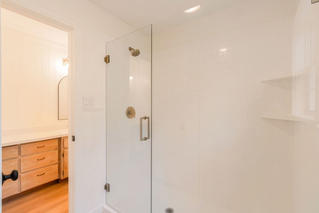 Shower enclosure with clear glass door, brushed brass fixtures, white subway tile surround, and integrated shelving