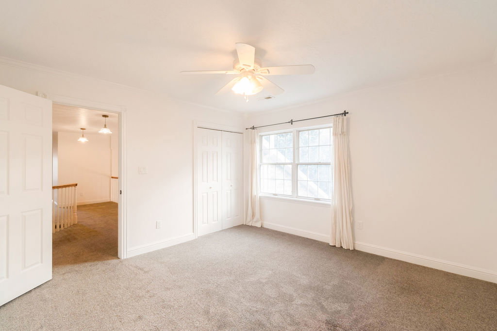 Bright interior room featuring a ceiling fan with integrated lighting, a double window with curtain rods, and neutral carpeting