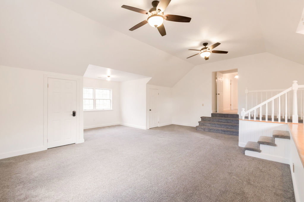 Spacious room featuring vaulted ceilings, two ceiling fans, and neutral-toned carpeting
