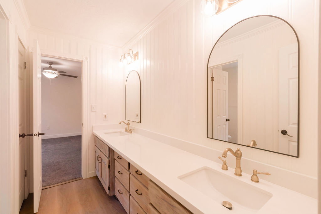 Double vanity featuring light wood-finish cabinetry, white countertops, and dual arched mirrors