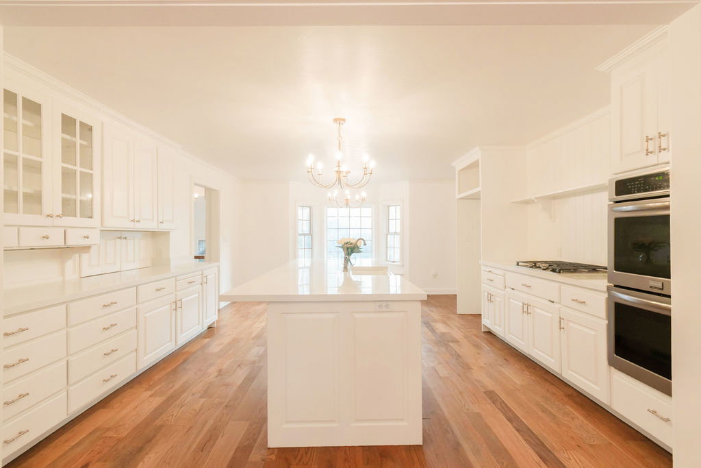 Expansive kitchen featuring white cabinetry, a large central island with a solid surface countertop, wood-finish flooring, a stainless steel double oven, and a gas cooktop