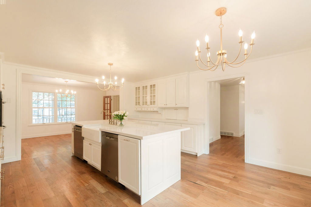 Spacious kitchen featuring a large central island with an apron-front sink, stainless steel dishwashers, white cabinetry, and light-toned countertops