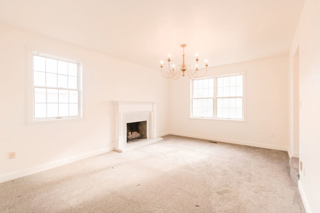Spacious room featuring a central fireplace with white mantel, two large windows with grid patterns, and a brass-finish chandelier