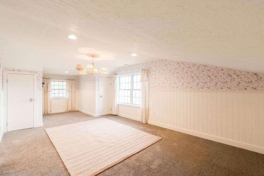 Spacious interior room featuring warm-toned carpeting and multiple windows