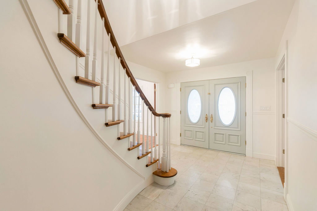 Foyer featuring a curved staircase with wood-finish handrail and balusters, double entry doors with oval glass inserts, recessed paneling, and marble flooring