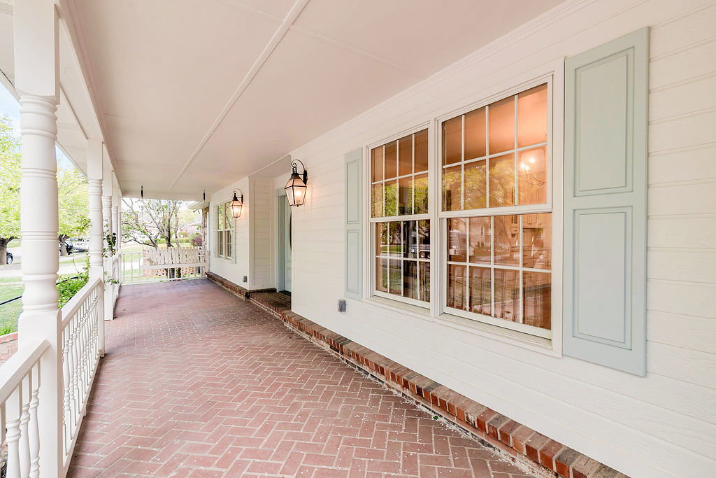 Expansive covered front porch featuring herringbone brick flooring, crisp white columns, and a matching balustrade