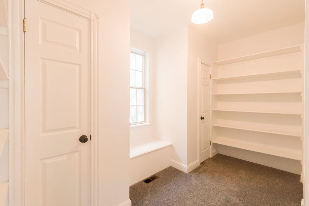 Built-in shelving for storage, window with integrated seating, wall-mounted lighting fixture, paneled doors, and carpeted flooring