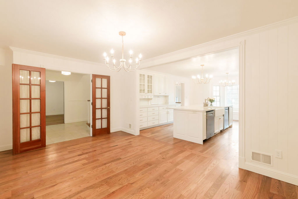 Open-concept design featuring wood-finish flooring, white paneling, and an elegant chandelier