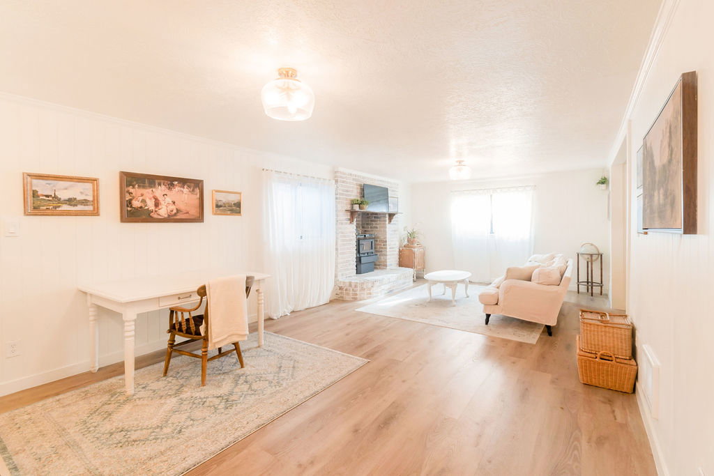 Spacious living area featuring wood-finish flooring, white paneling, and a brick fireplace