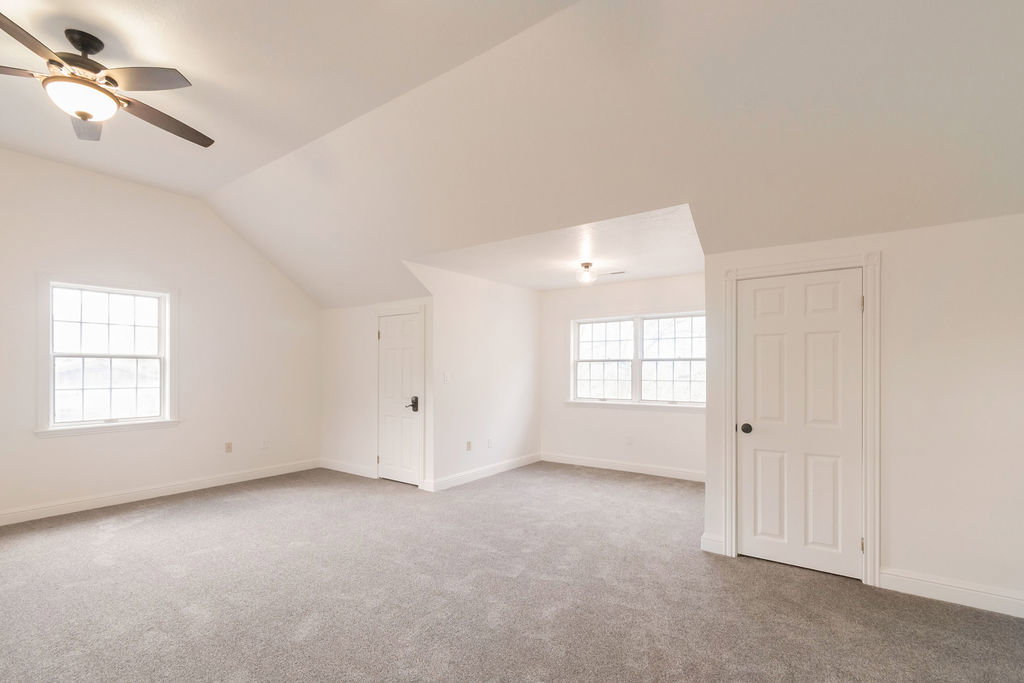 Spacious room with sloped ceilings, light gray carpet, multiple windows, and a ceiling fan with integrated lighting