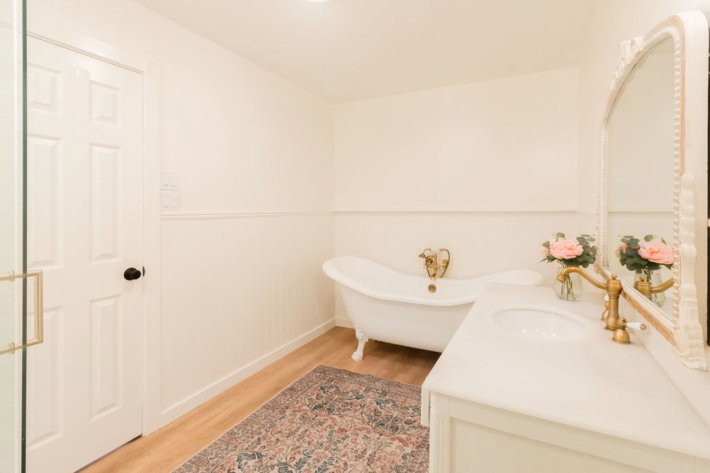 Clawfoot tub with antique brass fixtures, white vanity with integrated sink, and an ornate framed mirror